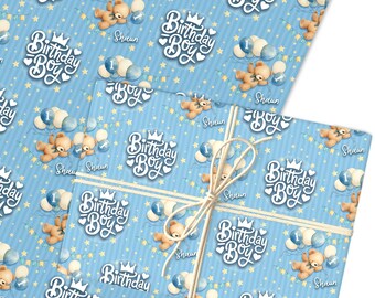 May include: Blue wrapping paper with a repeating pattern of teddy bears, balloons, and the text "Birthday Boy." The paper is tied with twine. The design includes stars and the name "Shaun."