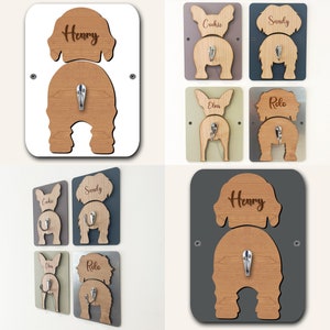 Op de afbeelding: Set van zes houten hondenpoot haken met de namen "Henry", "Cookie", "Sandy", "Elvis", "Rolo" erop gegraveerd. De haken zijn gemonteerd op verschillende gekleurde achtergronden: wit, grijs, bruin, groen en zilver.