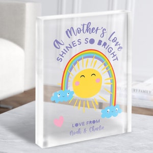 May include: A clear acrylic block with a rainbow, sun, and clouds design. The text reads "A Mother's Love Shines So Bright" and "Love From Noah & Charlie".