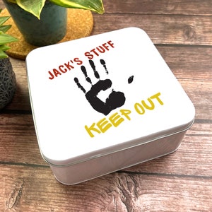 Könnte beinhalten: Weiße Metalldose mit einer roten und gelben Grafik, auf der "Jack's Stuff" steht, und einem schwarzen Handabdruck mit den Worten "Keep Out" in Gelb.