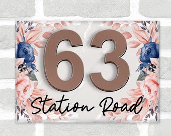 May include: Rectangular house number sign with the number 63 in bronze, and the words "Station Road" in black script. The sign is decorated with pink and blue floral accents on a white background.