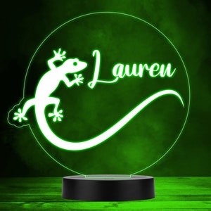 Può includere: Un geco bianco con una coda arricciata e il nome "Lauren" in un font bianco corsivo su uno sfondo verde. L'immagine è una rappresentazione 3D di una luce notturna.