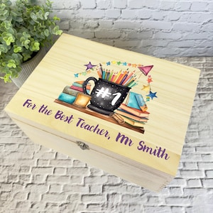 May include: Wooden box featuring a colourful illustration of a mug filled with pencils, books, and stars. The text "For the Best Teacher, Mr. Smith" is printed on the box.