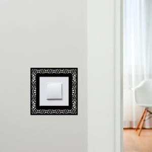 Peut inclure: Un interrupteur blanc encadré d'un cadre décoratif carré noir avec un motif géométrique. L'interrupteur est monté sur un mur blanc. Le cadre ajoute une touche moderne à l'installation électrique.