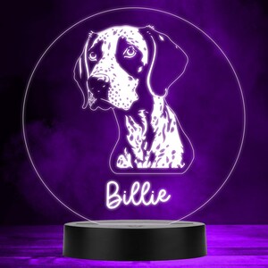 Op de afbeelding: Een wit en zwart silhouet van een hond met de naam "Billie" eronder. Het silhouet staat op een ronde, doorzichtige acrylbasis met een zwarte basis.