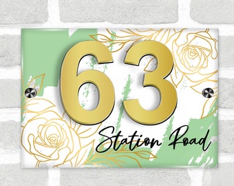 May include: A green and white house number sign with gold numbers 63 and the text "Station Road" in black cursive writing. The sign has a floral design with white roses and gold accents.