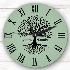 May include: A green round clock with black Roman numeral hour markers and black hands. The clock face features a black silhouette of a tree with roots and the text "Smith Family".