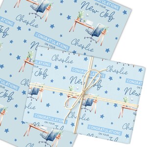 May include: Light blue wrapping paper with a repeating pattern of office desks, chairs, and stars. The text "Congratulations on Your New Job" and the name "Charlie" are also printed on the paper. A wrapped gift is tied with twine.
