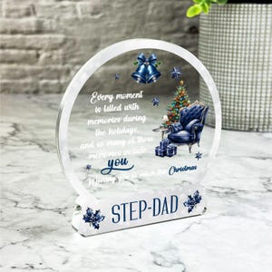 May include: A clear glass ornament with a blue and white Christmas tree, a blue armchair, and a message that reads "Every moment is filled with memories during the holidays. And so many of those memories include you. Missing you so much this Christmas." The ornament also has the words "STEP-DAD" on the base.