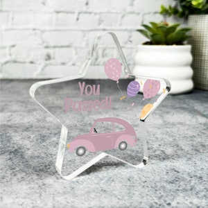 May include: A clear acrylic star-shaped paperweight with a pink car, balloons, and the text "You Passed!" printed on it.