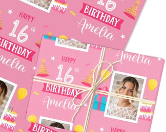 May include: Pink wrapping paper with a birthday theme. The design includes the text "Happy 16th Birthday Amelia", a photo, cake, party hats, and balloons. The wrapped gift is tied with twine.