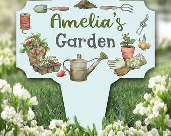 Può includere: Un cartello da giardino blu e bianco con il testo "Amelia's Garden" in lettere verdi e grigie. Il cartello presenta illustrazioni di attrezzi da giardinaggio, piante e un annaffiatoio.