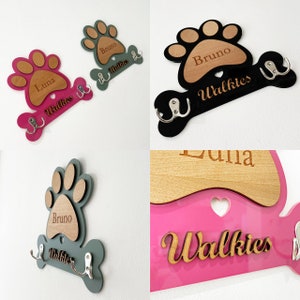 May include: Three wooden dog paw print key hooks with bone-shaped hangers. The hooks are painted in pink, black, and green. The paw prints have the names "Luna", "Bruno", and "Bruno" engraved on them. The bone-shaped hangers have the word "Walkies" engraved on them.