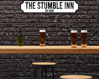 May include: A wooden sign with white lettering that reads "The Stumble Inn Est 2020" hangs above a bar counter with three glasses of beer and a bottle of beer. Two bar stools are in the foreground.