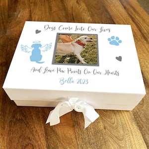 May include: White keepsake box with a photo of a dog, a paw print, a heart, and the text "Dogs Come Into Our Lives And Leave Paw Prints On Our Hearts Bella 2023".