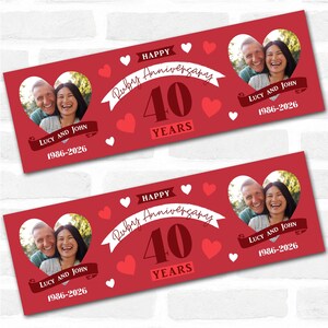 May include: Two red banners with a white brick background. Each banner features a photo of a couple in a heart-shaped frame, with the text "Happy Ruby Anniversary 40 Years" and the names "Lucy and John" with the dates "1986-2026".