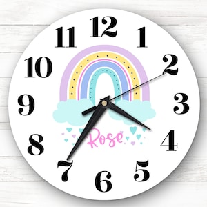 Może przedstawiać: Biały okrągły zegar z czarnymi cyframi i wskazówkami. Tarcza zegara przedstawia tęczę z chmurami i różowymi sercami. Imię "Rose" jest napisane różowym kolorem pod tęczą.