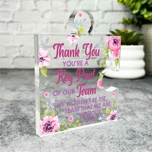 May include: A clear acrylic puzzle piece with a floral design and the text "Thank You You're a Key Part of Our Team We wouldn't be the team that we are without you".