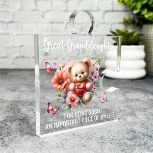 Puede incluir: Una pieza de rompecabezas de acrílico transparente con un diseño floral y un osito de peluche que sostiene un corazón que dice "Gracias". El texto en la pieza del rompecabezas dice "Bisnieta, por ser una parte tan importante de mi vida."