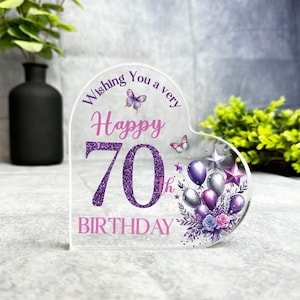 May include: Purple and pink heart-shaped acrylic sign with glitter accents. The sign reads "Wishing you a very happy 70th birthday" with butterflies and balloons.