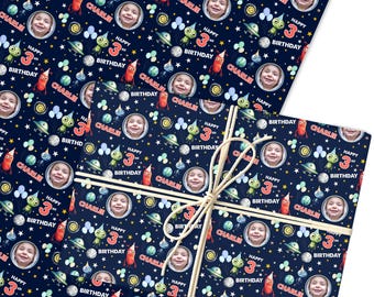 May include: Navy blue wrapping paper with a repeating pattern of a child's face, aliens, rockets, planets, and the text "Happy 3rd Birthday Charlie". The paper is tied with natural twine.