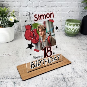 Può includere: Una cornice per foto in acrilico trasparente con una base in legno. La cornice presenta una foto di una persona con guantoni da boxe e il testo "Simon Happy 18th Birthday".