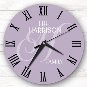 Può includere: Un orologio color lavanda con indicatori delle ore in numeri romani e lancette nere. Il quadrante dell'orologio presenta il testo "THE HARRISON FAMILY" in lettere bianche.