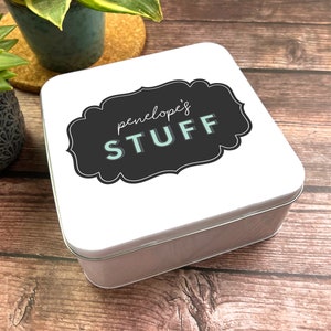 Peut inclure: Boîte en métal blanc avec une étiquette noire et blanche. L'étiquette a une bordure décorative et le texte "penelope's STUFF" en lettres blanches et turquoise.
