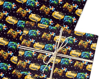 May include: Wrapping paper featuring a repeating pattern of colourful video game controllers, balloons, and stars on a dark background. The text "Happy 10th Birthday CHARLIE" is featured. The paper is tied with natural twine.