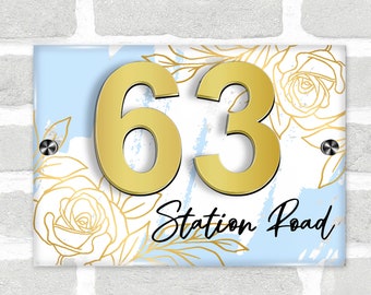 May include: A blue and white house number sign with gold floral accents and the number 63. The sign also includes the text "Station Road" in black.