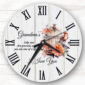 May include: A white wooden clock with Roman numerals and a black clock hand. The clock face features a watercolor illustration of a bird in a cage with flowers. The text "Grandma's" and "Like you are precious and you are one of a kind" is written on the clock face. The text "Love You" is written below the illustration.