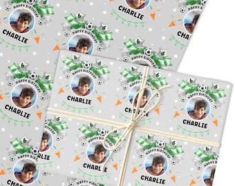 May include: Gray birthday wrapping paper featuring a repeating pattern of a child's photo, soccer balls, green star-shaped balloons, and the text "Happy Birthday" and "Charlie". The paper is tied with twine.