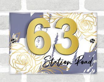 May include: A white and gray house number sign with gold numbers 63 and the text "Station Road" in black script. The sign has a floral design with white roses and gold leaves on a purple background.