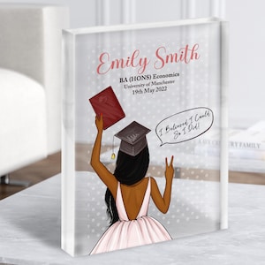 May include: A graduation keepsake featuring a black woman in a pink dress and graduation cap, holding a red diploma and making a peace sign. The text reads "Emily Smith, BA (HONS) Economics, University of Manchester, 19th May 2022, I Believed I Could, So I Did!"