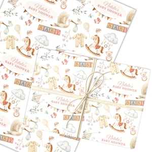 May include: Baby shower-themed wrapping paper. The design includes illustrations of a stork, rocking horse, baby clothes, and blocks spelling "BABY." The text "Natalie's BABY SHOWER" is visible. The paper is tied with twine.