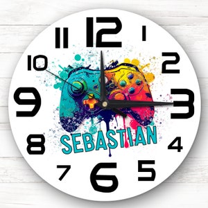 Könnte beinhalten: Weiße runde Uhr mit schwarzen Zahlen und Zeigern. In der Mitte der Uhr befindet sich ein bunter Videospiel-Controller mit dem Namen "SEBASTIAN" darunter.