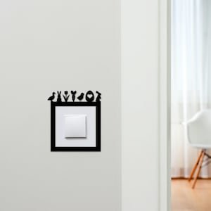 May include: Black decorative light switch cover with Easter-themed silhouettes. The design includes a bird, bunny, tulip, carrot, chick, egg, and heart. The cover is mounted on a white wall, with a white light switch in the center.