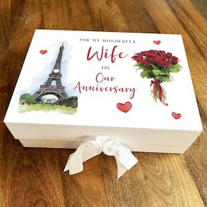May include: White gift box with a red ribbon. The box has a watercolor illustration of the Eiffel Tower and a bouquet of red roses. The text on the box reads "For my wonderful Wife on our Anniversary".