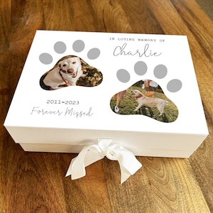 May include: White box with a paw print design and two photos of a dog. The box has a white ribbon and the text "In loving memory of Charlie 2011-2023 Forever Missed".