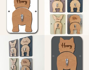 Puede incluir: Conjunto de seis ganchos de madera con forma de trasero de perro con los nombres "Henry", "Cookie", "Sandy", "Elvis", "Rolo" grabados en ellos. Los ganchos están montados sobre fondos de diferentes colores: blanco, gris, azul claro, verde, plateado y gris oscuro.