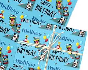 May include: Light blue wrapping paper featuring a race car design. The pattern includes race cars, balloons, trophies, and the words "Happy Birthday" and "Matthew". The paper is tied with twine.
