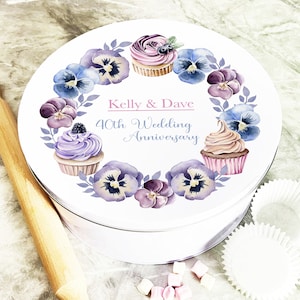 Könnte beinhalten: Weiße runde Kuchenform mit einem violetten und blauen Blumendesign und zwei Cupcakes. Der Text "Kelly & Dave 40th Wedding Anniversary" ist auf der Form aufgedruckt.