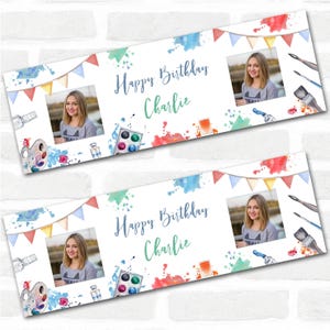May include: A banner with a watercolour design, featuring a photo, paint palette, brushes, and the text "Happy Birthday Charlie." The banner has a white background with colourful paint splatters and pennant flags.