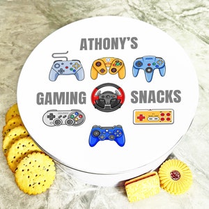 Op de afbeelding: Witte ronde blik met de tekst "ATHONY'S GAMING SNACKS" en afbeeldingen van verschillende videogamecontrollers.