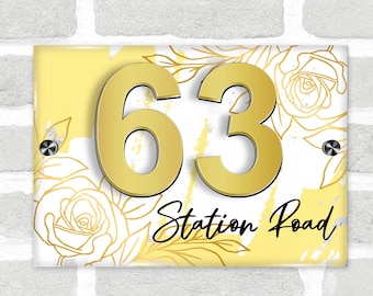 May include: A yellow and white house number sign with gold floral accents and the number 63. The sign also includes the text "Station Road" in gold lettering.