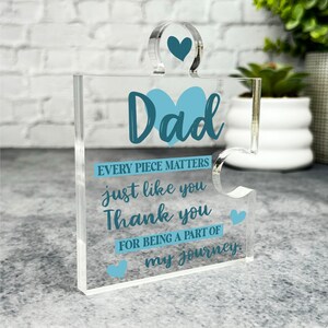 Può includere: Un pezzo di puzzle in acrilico trasparente con un cuore blu e la parola "Dad" in lettere blu. Il testo "EVERY PIECE MATTERS just like you Thank you FOR BEING A PART OF my journey." è stampato sul pezzo di puzzle.