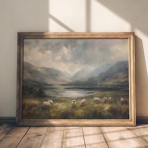 May include: A framed oil painting depicting a landscape scene with a lake, mountains, and sheep grazing in a field. The painting is set against a light brown wall with a shadow cast from a window.