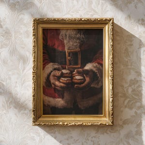 May include: A framed print depicts Santa Claus holding two cookies. The artwork features Santa's red coat with white fur trim, a black belt with a gold buckle, and his hands holding the treats. The frame is gold with ornate detailing.