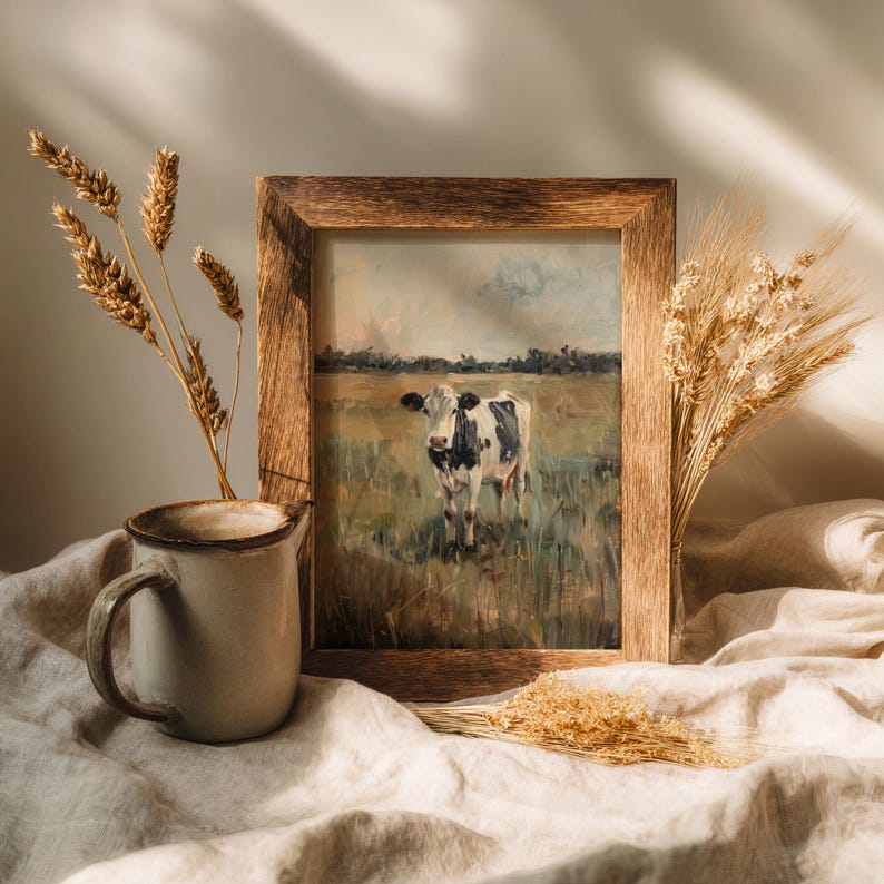 Cow printable artwork in rustic wooden frame, placed on linen fabric with ceramic mug and dried grass, soft farmhouse aesthetic