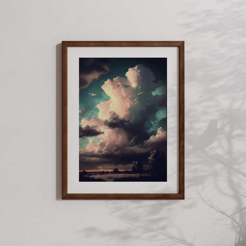 May include: A framed print of a landscape with a large, fluffy, pink and white cloud in a blue and green sky. The cloud is casting a shadow on the ground below.